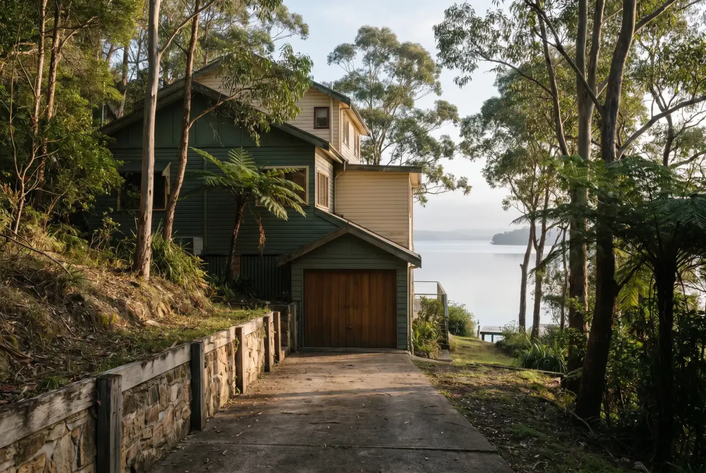 An under-house garage at the bottom of a steep concrete driveway, set below road level on a sloping block